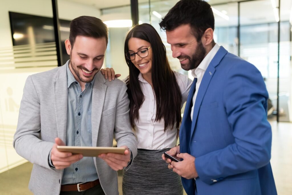Trois professionnels souriants regardant ensemble une tablette dans un bureau moderne, représentant le travail d'équipe et la collaboration