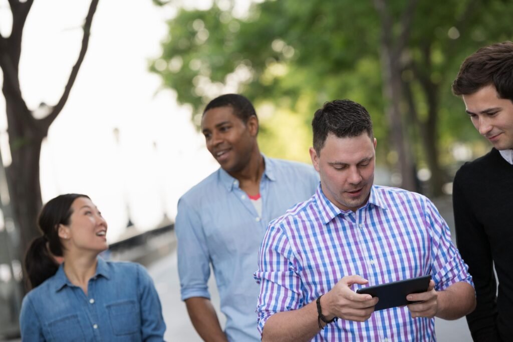 Un groupe de quatre collègues marchant ensemble en plein air, l'un utilisant une tablette, symbolisant le travail d'équipe et la technologie.