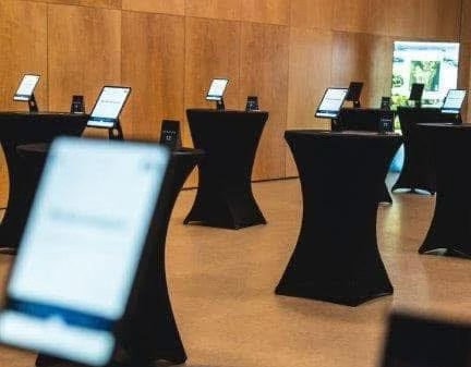 Una habitación espaciosa preparada para un evento de construcción de equipos, con varias mesas altas con tabletas colocadas en la parte superior. El acuerdo enfatiza la organización y un enfoque en las actividades interactivas basadas en la tecnología.