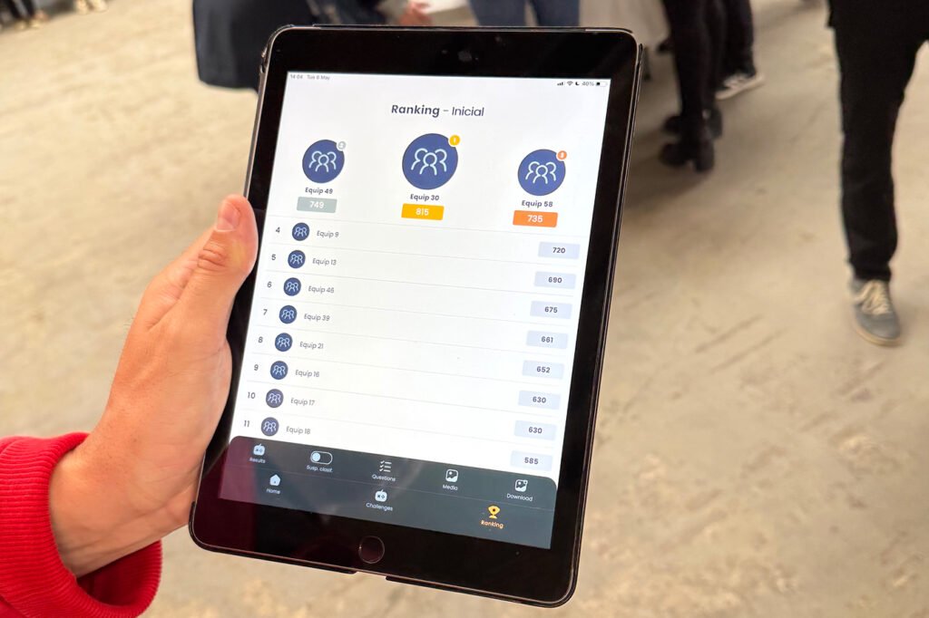 Participant holding a tablet displaying Mooveteam’s live ranking screen (‘Ranking – Inicial’) with team names and scores during a corporate event setup.